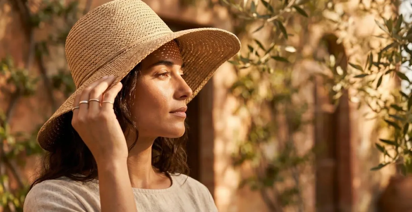 Una persona si protegge dal sole estivo con un cappello a tesa larga in un contesto mediterraneo.